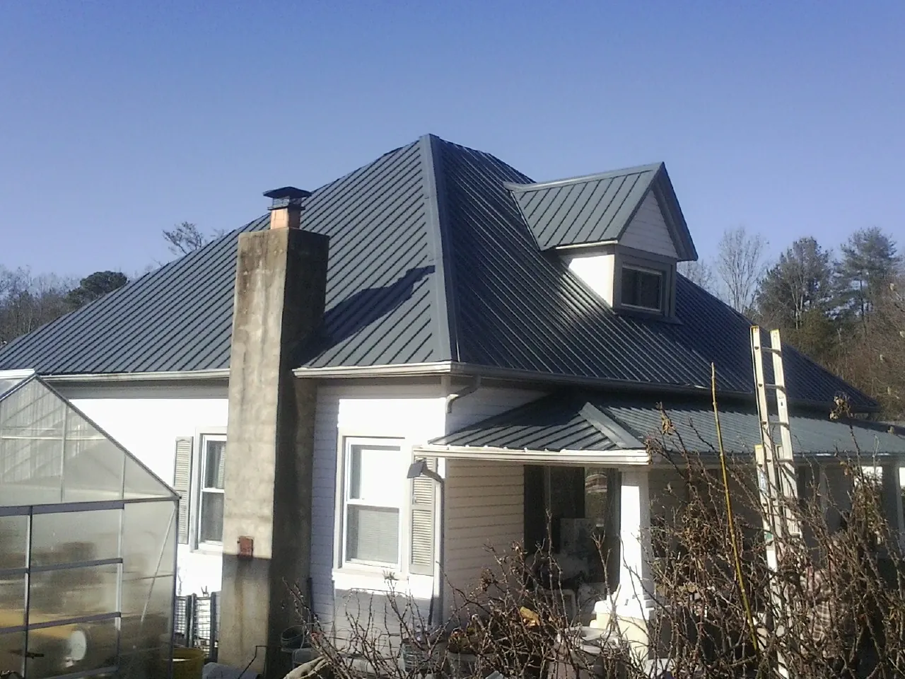 Dark blue standing seam metal roof on a white farmhouse with dormer — Slate & Tile Roof Repair by Roofing Brothers in San Marcos