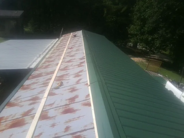 Old rusted panels beside newly installed green metal roofing — Wind Damage Roof Repair by Roofing Brothers in San Marcos