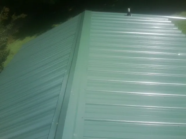 New green metal panels meeting at the ridge of a roof — Flat Roof Repair work by our crew in San Marcos
